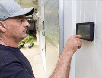 Un homme portant une casquette interagit avec un écran tactile fixé au mur dans une serre.