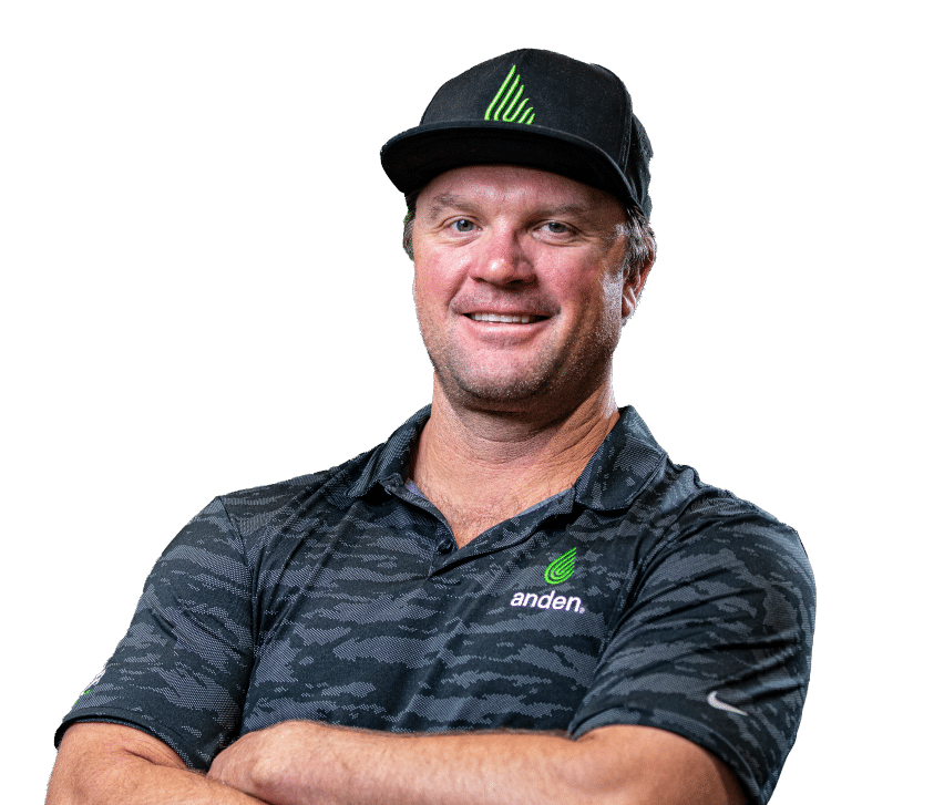 Homme souriant, vêtu d'un polo et d'une casquette camouflage noirs à logo vert, les bras croisés sur fond vert uni.