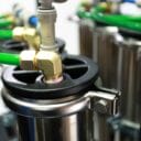 Brass fittings connect green hoses to metallic canisters, showcasing industrial equipment in a close-up view.