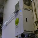 Anden dehumidifier mounted on a wall, featuring a green logo and digital control panel, with pipes connected below.