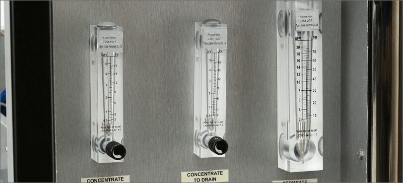 Trois débitmètres transparents montés sur un panneau métallique, étiquetés pour concentré, vidange et concentré à vidange.