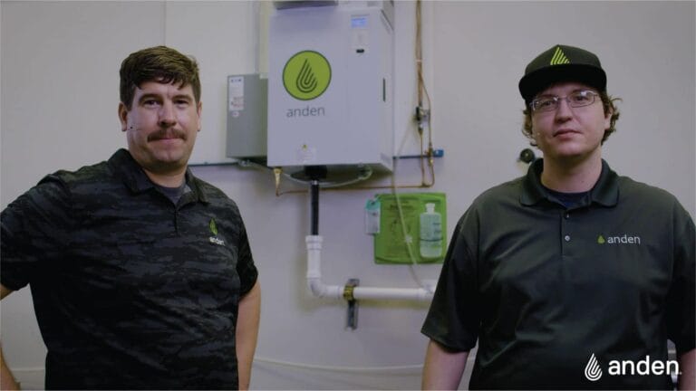 Two men in branded shirts stand in front of a wall-mounted device, showcasing a clean, professional workspace.