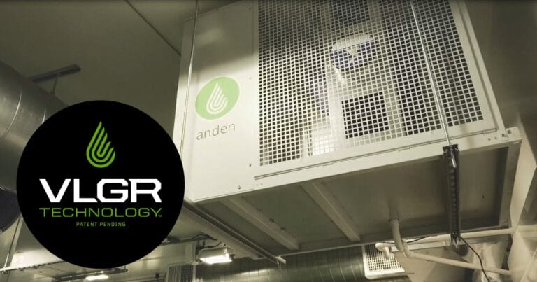 Anden dehumidifier mounted on a wall, featuring a green logo, with ventilation ducts visible in the industrial setting.